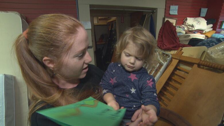 A woman stands with a young girl in her arms. The girl is holding a green handmade card.