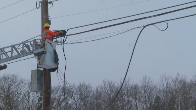 A worker in the bucket of a ladder truck works on overhead lines.