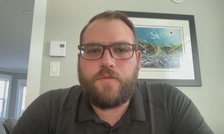 A head and shoulders shot of a person sitting inside, wearing glasses and a polo shirt.