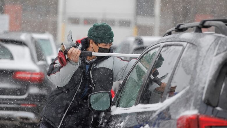 A man is pictured trying to clean a car windshield from falling snow. 