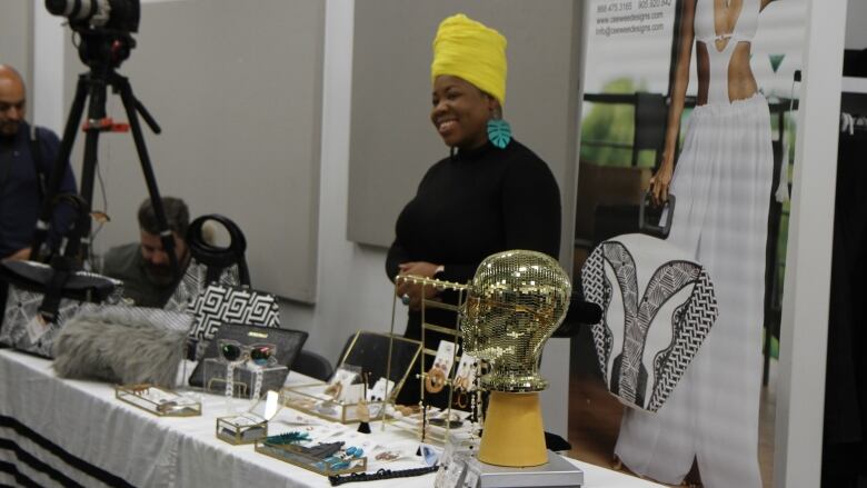 A woman smiling and standing behind a table with various accessories on it.