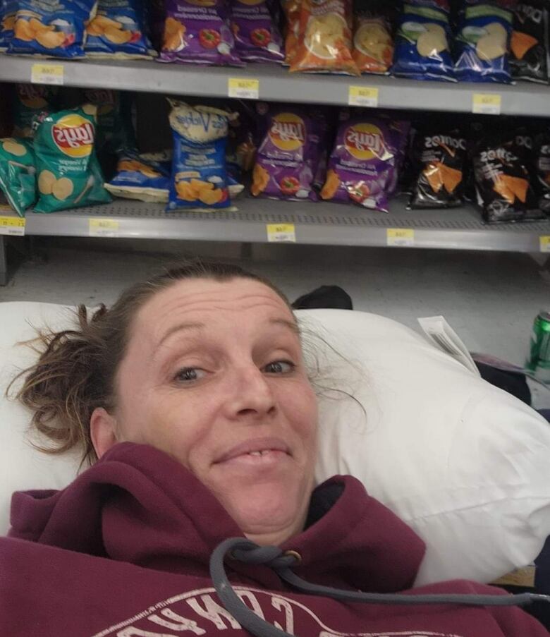 A woman lies on an air mattress with chips on the shelves behind her.