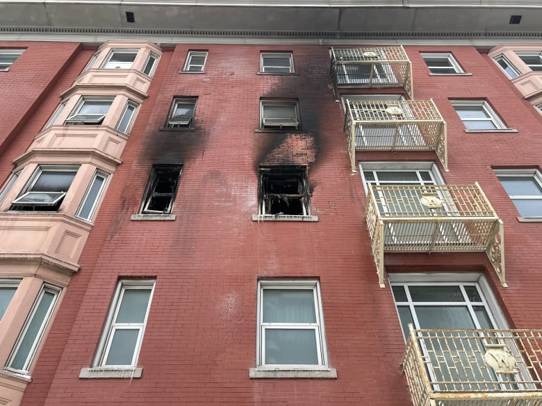 Charred windows, missing glass, on a red-brick apartment building.