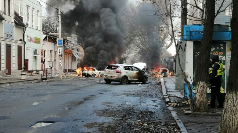 Grey smoke billows from burning cars on a commercial road.