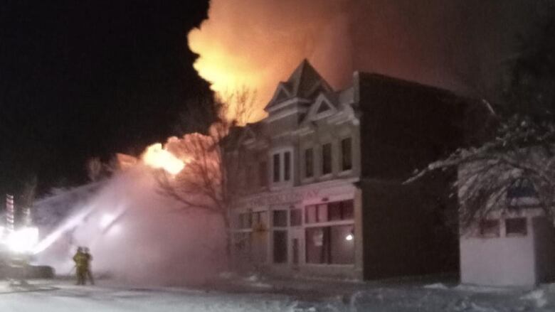 Firefighters on a snow-packed street douse a heritage building engulfed in flames, at night.