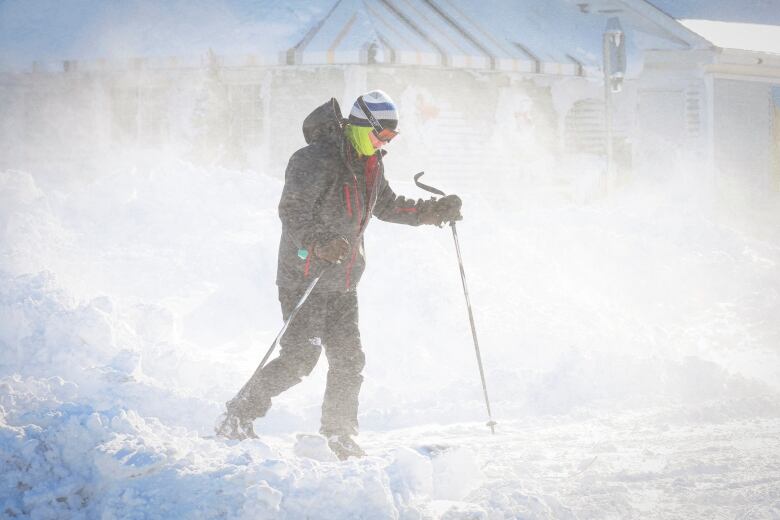 A man holding ski poles traverses along a snowy terrain.