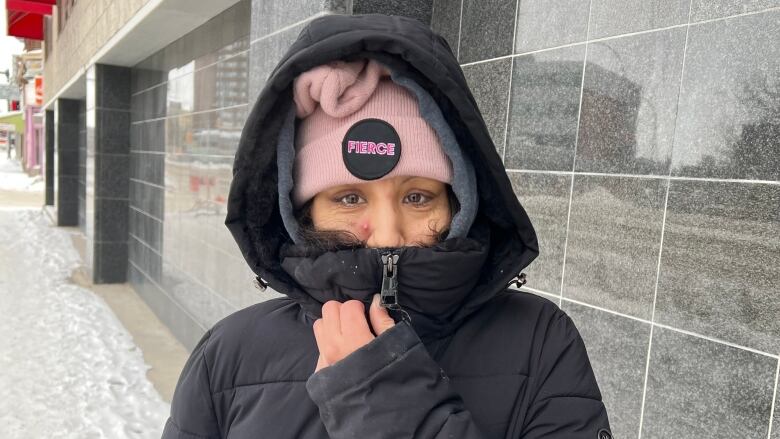 A woman stands outside with a pink toque.