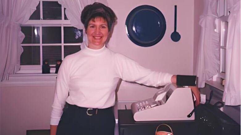 A woman stands beside a cash register and smiles at the camera