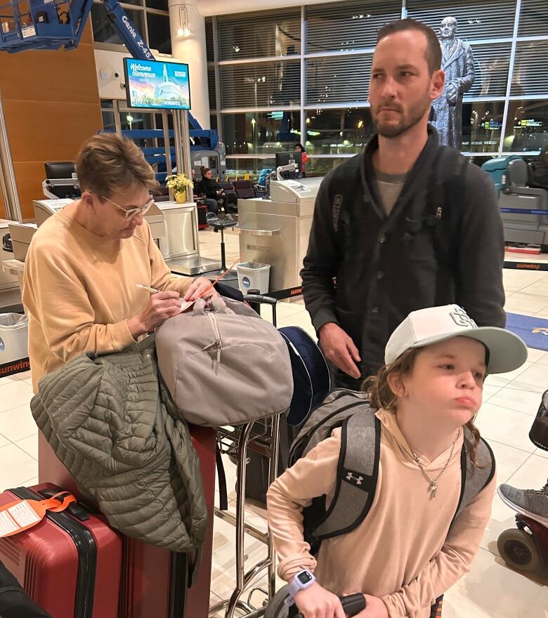 Two adults and a child stand at an airport with a number of bags.