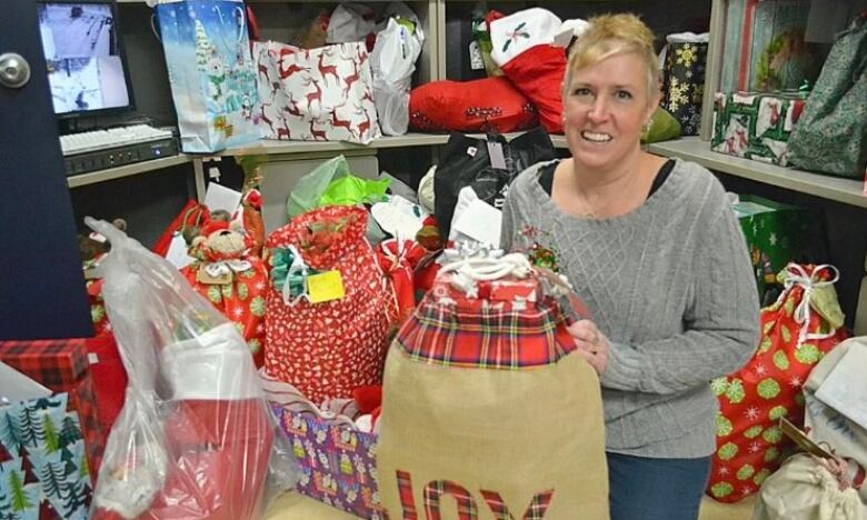 A woman stands around gift bags holding a gift. 