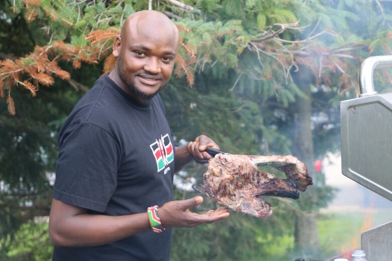 A Black man is in front of a barbecue, holding up a piece of meat with a pair of tongs. 