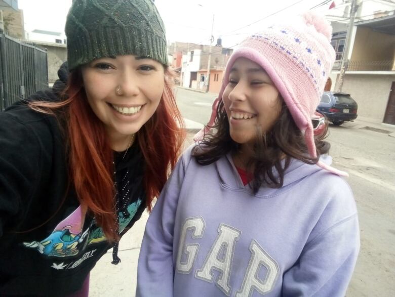 A woman is seen wearing a dark grey beanie next to a young girl wearing a purple hoodie and a pink winter hat. Both are smiling.