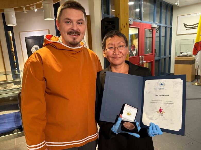 Two smiling people, one holding open a folio.