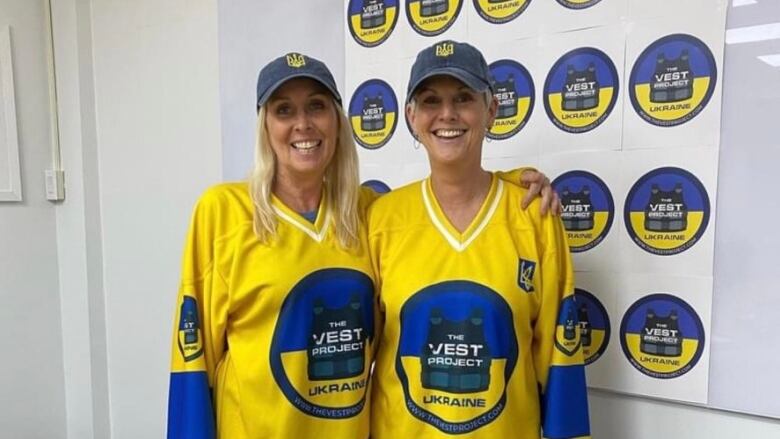 Two women wearing yellow and blue jerseys standing in front of yellow and blue sign