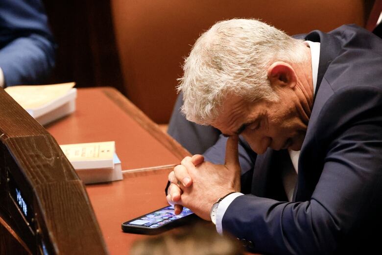 Man with his head bowed down on a desk in front of him. 