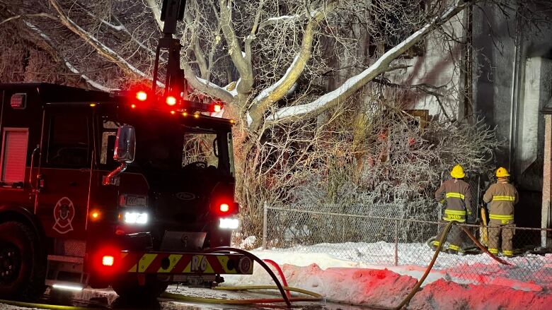 Two firefighters stand in a yard, facing a house.