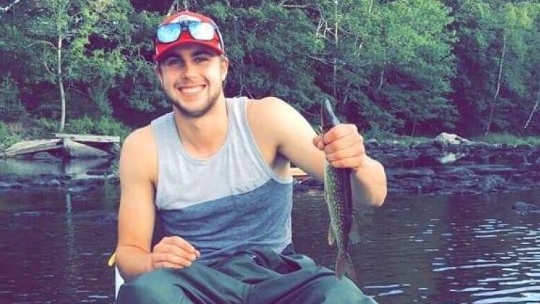 A smiling man sits on a boat holding a fish.