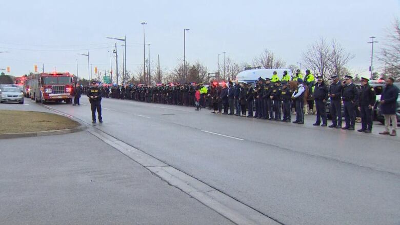 Men and women in police uniforms standing in line across a road.