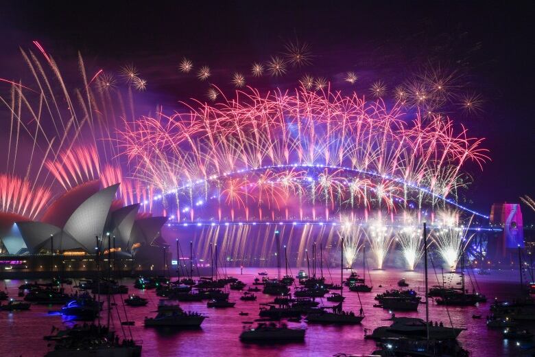 Fireworks explode in fuschias and purples over the Sydney Opera house and boats in Australian New Year celebratinos