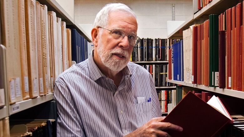 Alan Ruffman is seen holding a folder with shelves of books in the background.