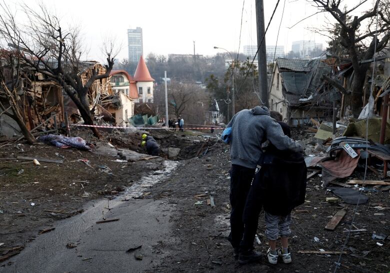 A person and a child embrace near rubble following a missilestrike.