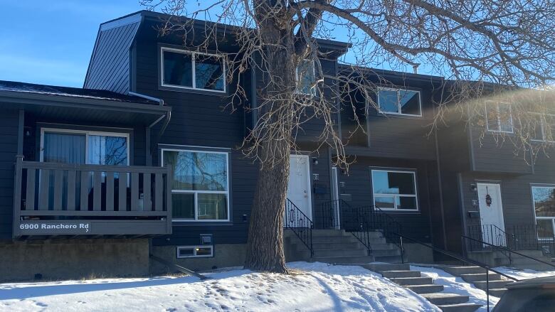 A police vehicle is parked outside a dark blue condo building outside of which is a large tree and snow on the ground. 