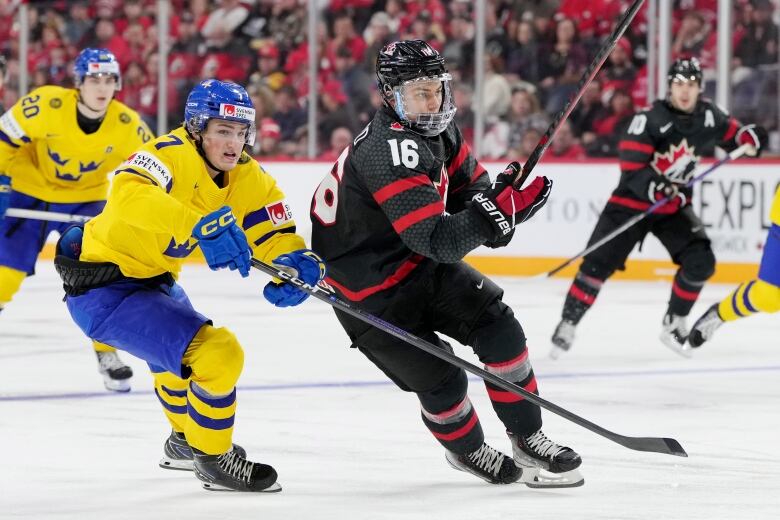 A Canadian hockey player tries to separate from a Swedish player as they chase the puck.