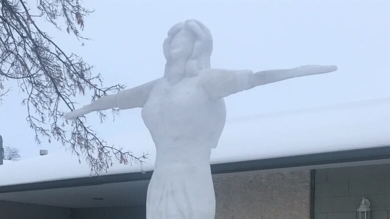 A tall snow sculpture of a woman with her arms out looking towards the sky.