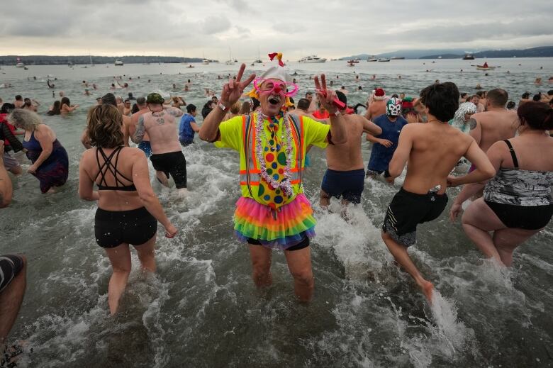 A person wearing a colourful costume including a tutu gives the peace sign during a Polar Bear Swim on New Year's Day.