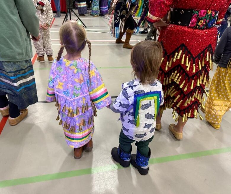 A young girl and boy with their back to the camera hold hands.