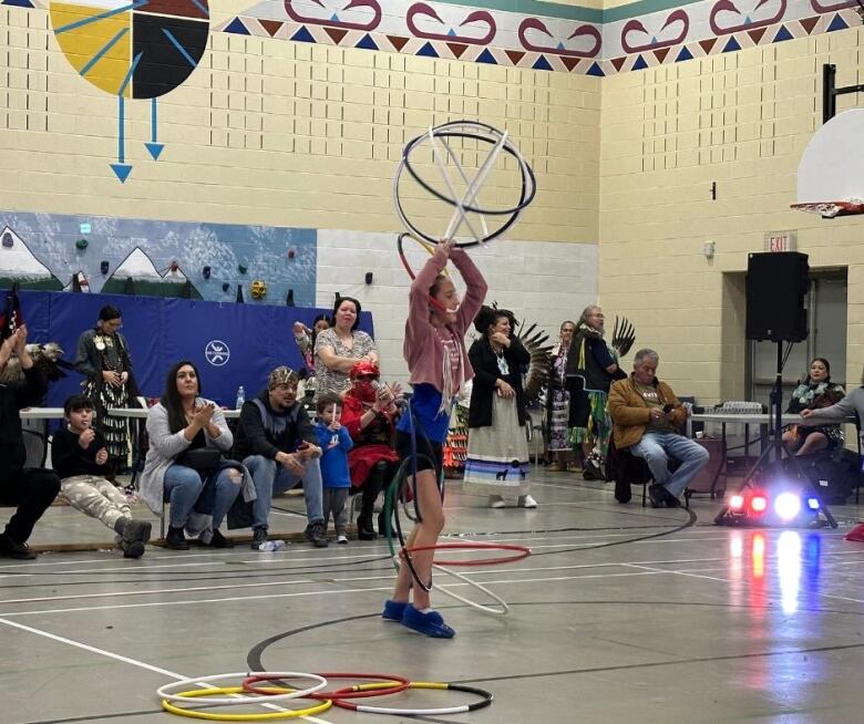 A girl holds several hula hoops above her head as she performs a dance in a gym.