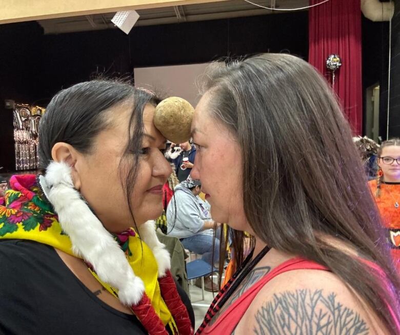 Two women face each other with a potato pressed between their foreheads. 