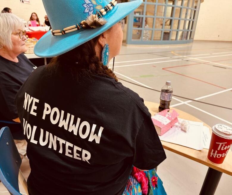 A woman wears a t-shirt that says 'NYE POWWOW VOLUNTEER'