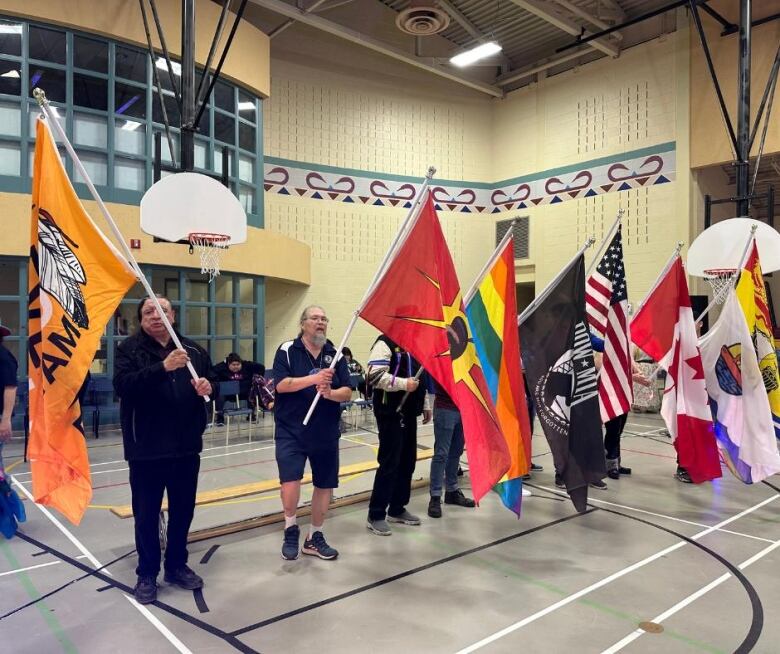 A group of people stand in a line inside a gym, each holding up a different flag.