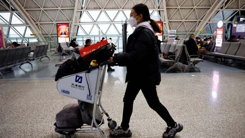 An individual wearing a mask walks with a luggage cart.