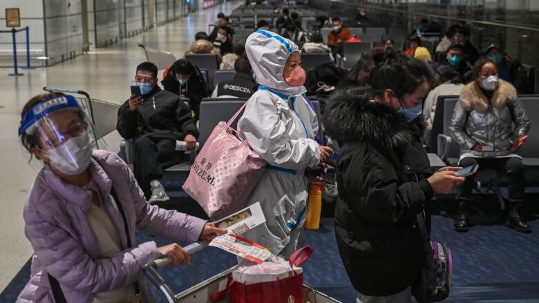 People in masks are shown at an airport departure lounge.  