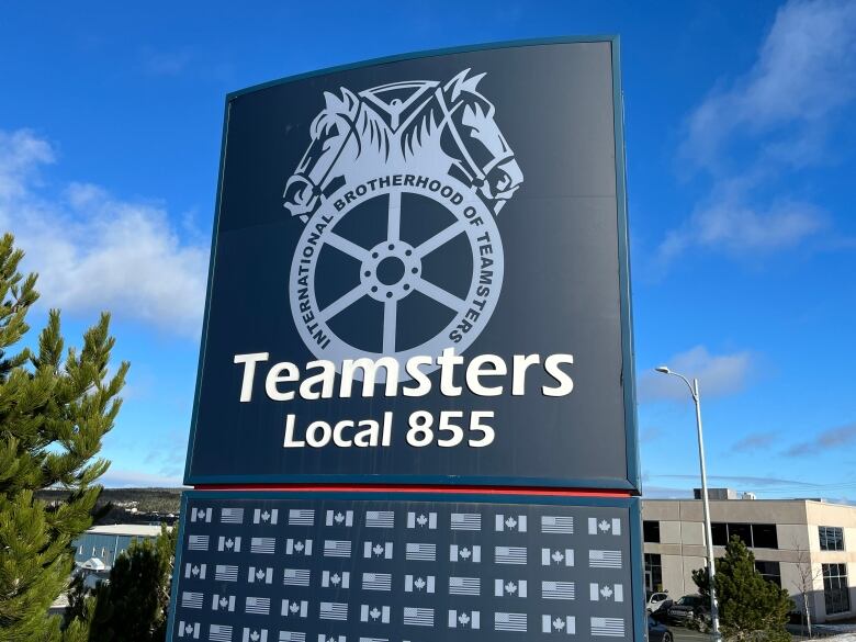 A large metallic sign stands on the lawn of a building.