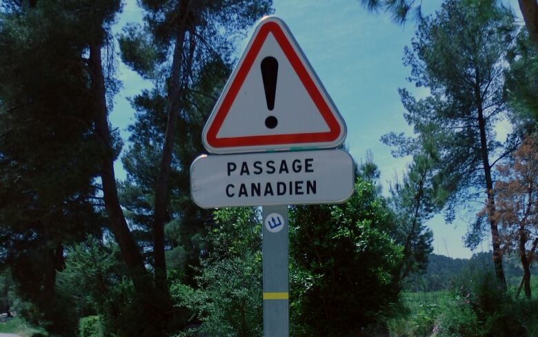 A yield shaped road sign in red and white with writing that reads Passage Canadien.