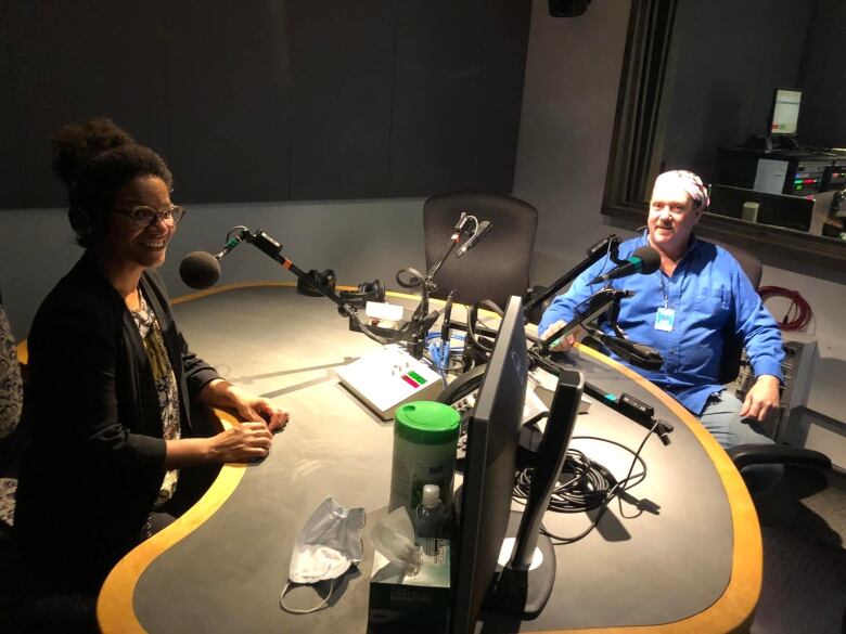 A woman and man sit around a table in a radio studio. 