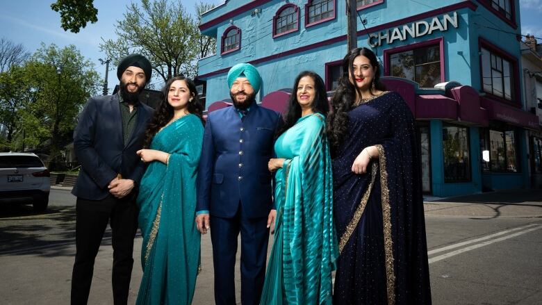 The Singh family stands  on the streetin front of their shop in Toronto's Little India. Son Chandan, daughter Chandni, father Kuki, mom Sarab and daughter-in-law Roop. The family is dressed in blue saris and blue suits. 