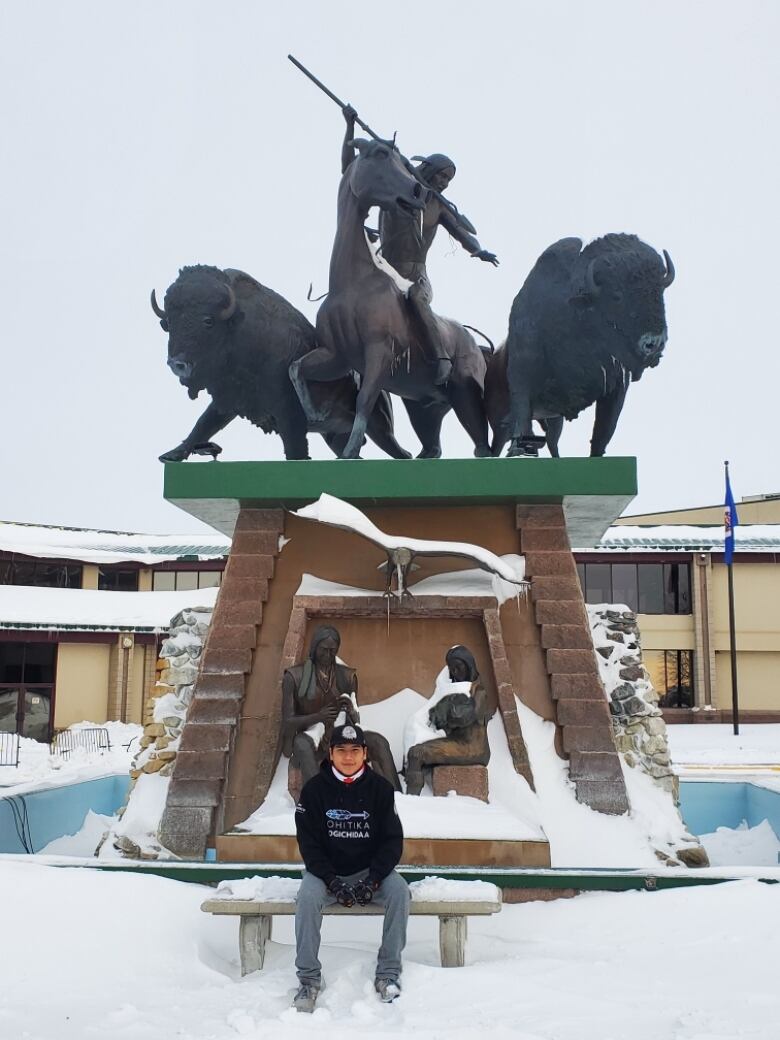 A young man sits in front of a bronze statue depicting Dakota warriors.