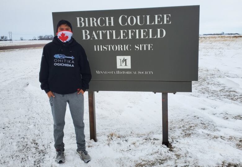 A boy stands in a snowy field in front of a sign that says 