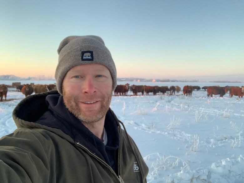 A man smiles in front of a herd of cows.