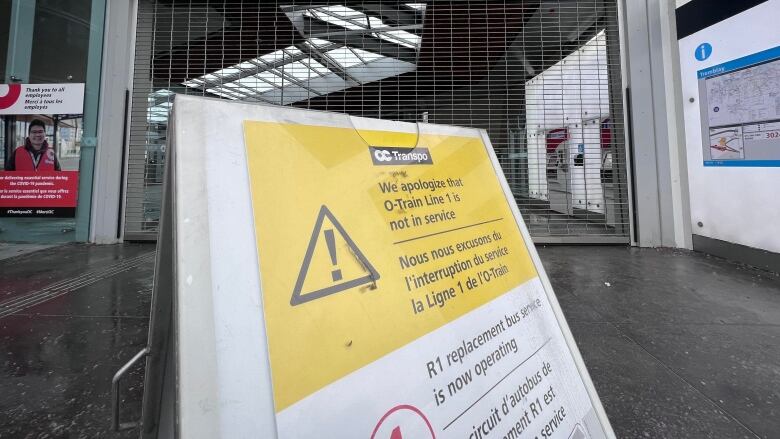 A temporary sign in front of a fenced-off transit station entrance. The sign tells people the light rail line is closed.