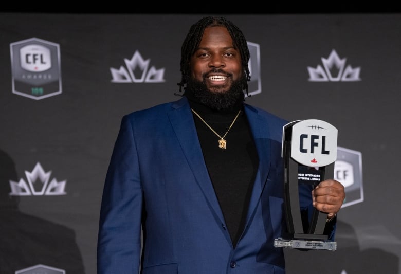 A man in a suit holds a CFL award and smiles at the camera