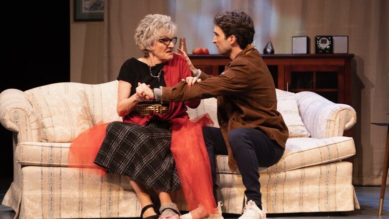 A young man and an older woman sit on a couch and appear to be having a difficult conversation.