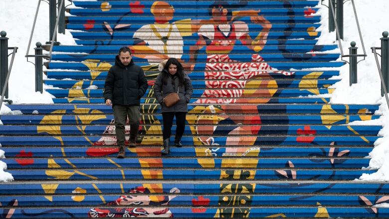 Two people walk down a set of stairs in winter. The stairs are decorated with an illustration of two people dancing.