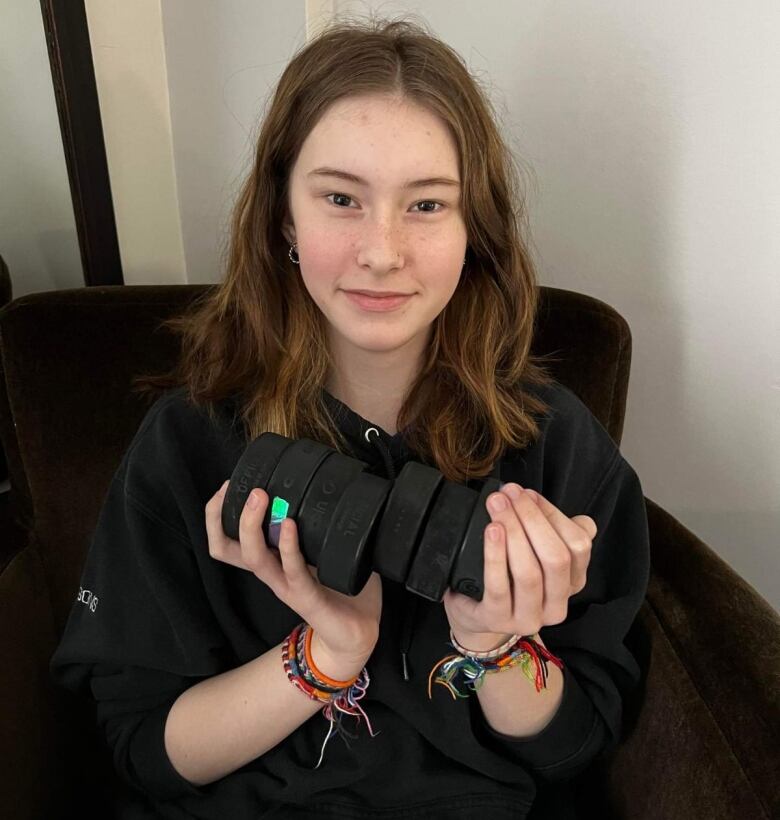 A girl holding eight hockey pucks sitting in a chair. 