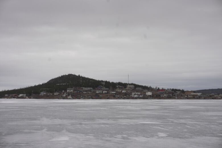 A frozen lake sits before a small community that has a hill in the background. 