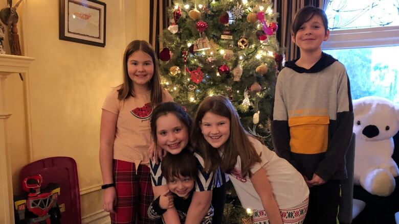 Children smiling in front of a sparkling Christmas tree